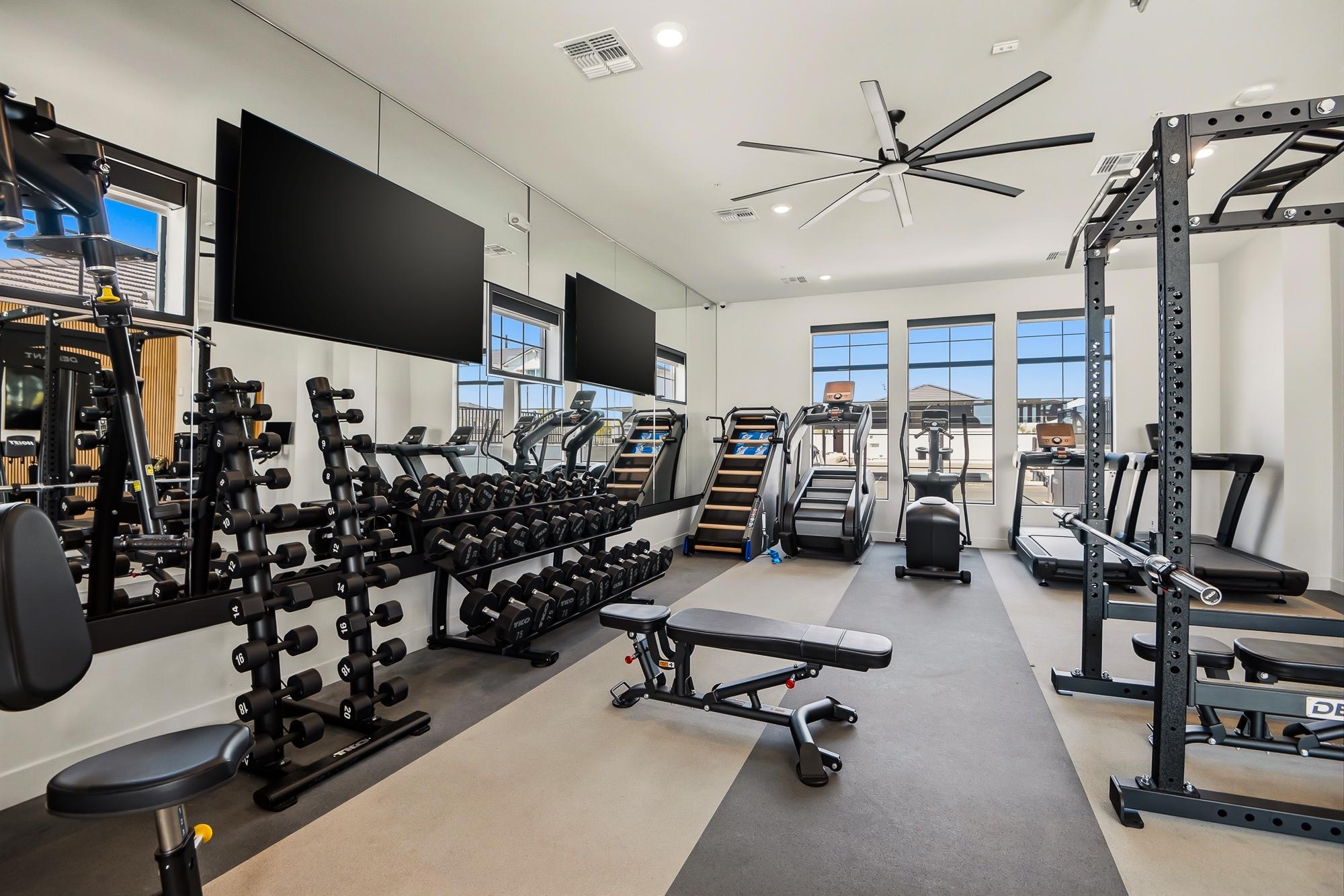 Modern gym with free weights, benches, cardio machines, and large windows letting in natural light.